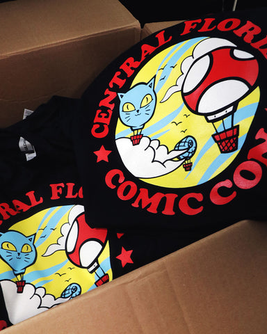 Camisas impresas con "Comic Con" y globos en una caja