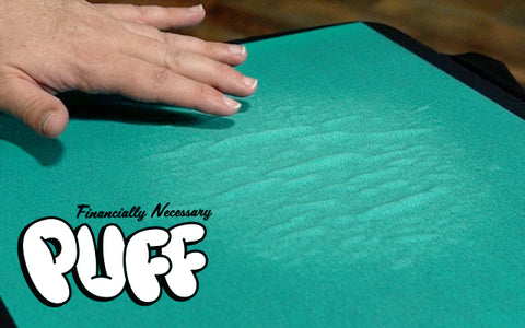 a hand hovers over a teal printed shirt with "puff" written in the bottom corner