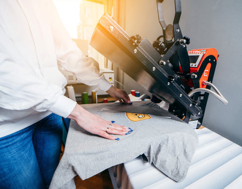 a hand holds a grey shirt down and heat presses it