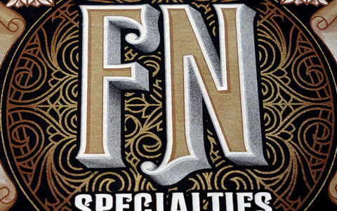 Una imagen de una impresión que lee "FN Specialties" con oro, plata, perla y hojaldre impreso en la prenda