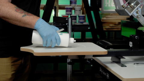 A hand wearing a glove pours water-based pallet adhesive onto a platen