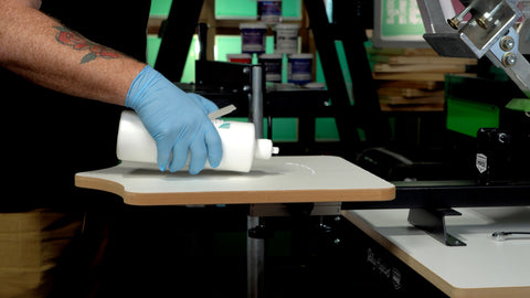 a gloved hand applies water-based pallet adhesive to a platen