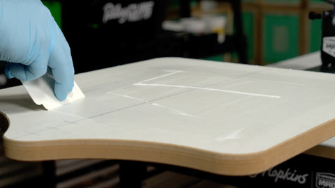 A gloved hand swipes water-based pallet adhesive around a platen using a cleanup card