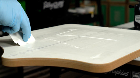 a hand swipes water-based pallet adhesive around a platen with a cleanup card