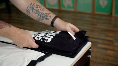 a man with tattoos folds a black shirt