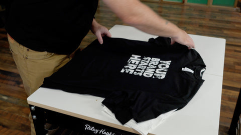 a man folds black shirts on a press cart