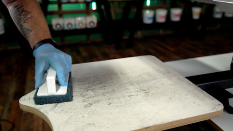 A gloved hand uses a scrub brush to clean lint off a platen
