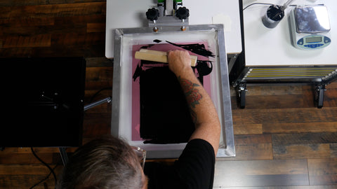 a printer leans over a press and prints black water-based ink