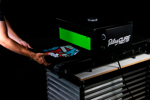 hands catch a shirt printed with blue and red as it comes out of a conveyor dryer