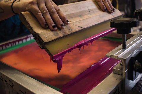 Two hands hold a squeegee with magenta ink