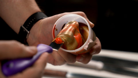 Mezcla de tinta naranja y dorada con una espátula de tinta en un recipiente