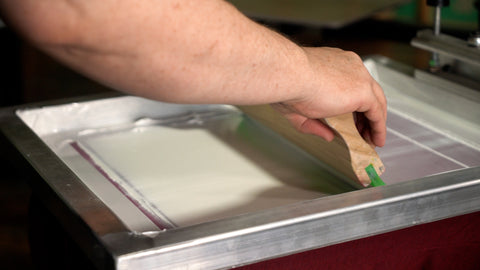 A screen printer pulls a squeegee down a screen