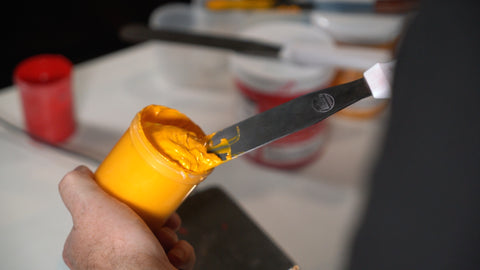 a container of yellow ink being mixed with an ink spatula