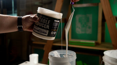 A bucket of curable reducer with ink coming out of it on a spatula