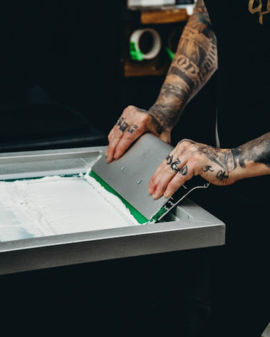 Two hands push a squeegee on a screen of white ink