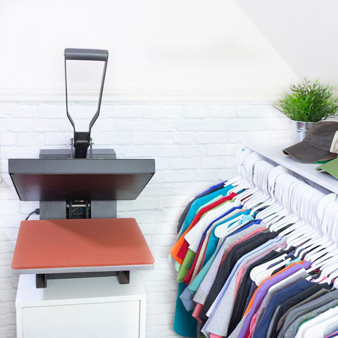 A heat press sits next to a rack of colorful shirts