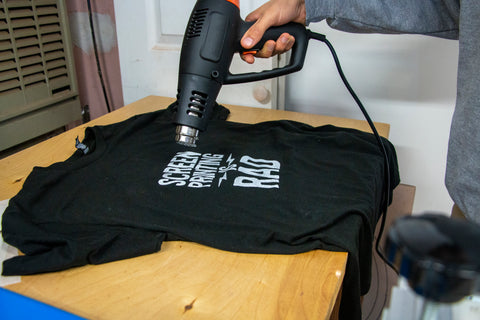 Una mano sostiene una pistola de calor sobre una camisa