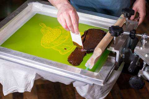 A hand spreads brown ink with coffee in it on a screen