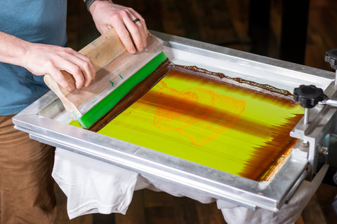 A printer pulls a squeegee of brown ink down a screen