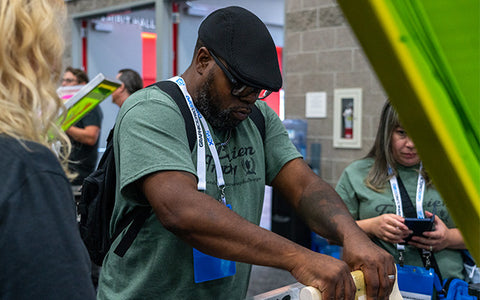 a man in a hat pulls a squeegee on a black shirt at the Graphics Pro Expo