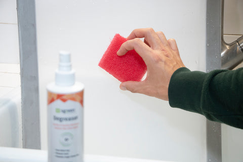 Una mano sostiene una esponja hasta una pantalla con productos químicos de limpieza sentados