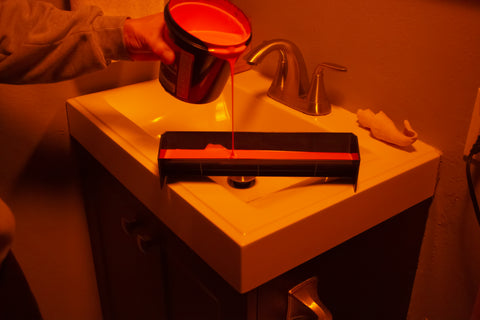 a person pouring emulsion into a scoop coater next to a sink