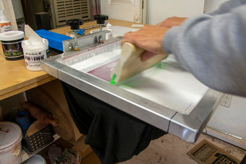 an arm pulls a squeegee down a screen on a blue press