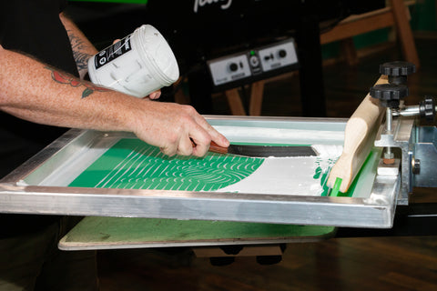 A hand places ink on a screen with a spatula