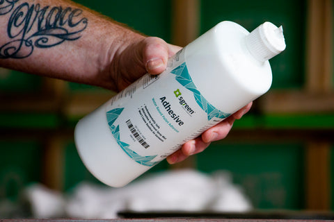 a hand holds a bottle of water-based pallet adhesive