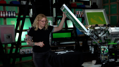 a woman with blonde hair stands in front of a press with the screen raised