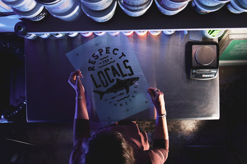 A person holds a film positive reading "respect the locals" with an image of a shark