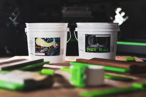 Two buckets of water based ink sit on a table with squeegees and other screen printing supplies