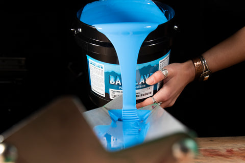 person pouring baselayr plastisol emulsion into a scoop coater