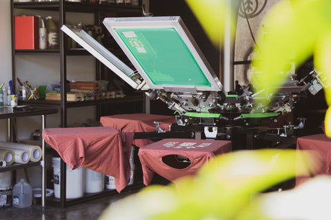 A manual printing press with all screens loaded and shirts on all the platens