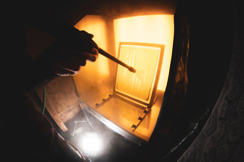 A hand holds a pressure washer and points it at a screen sitting in a washout booth