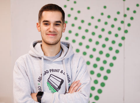 a man folds his arms and smiles in front of a green wall of halftones