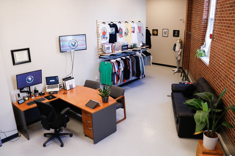 a screen printing shop office with a desk and rack of shirts