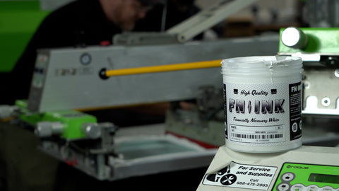a pin of FN-INK sitting next to an automatic screen printing machine