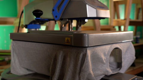 A heat press in use pressing a design onto a grey shirt