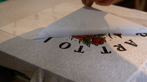 a hand peels transfer paper off a plastisol transfer onto a shirt
