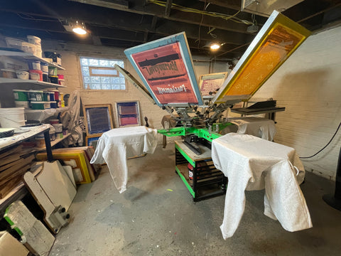 A Riley 250 screen printing press with screens in and shirts hanging on the platens