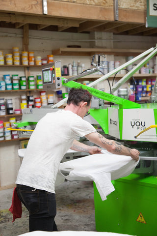 a man loads shirts onto an automatic screen printing machine