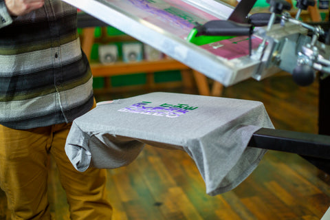 Un hombre sostiene una pantalla para revelar una camisa gris con diferentes colores de tinta impresos