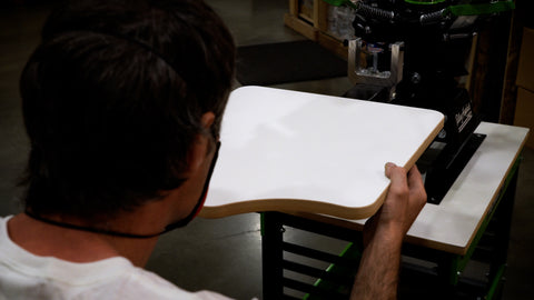 A man holds a wood platen up to a screen printing press