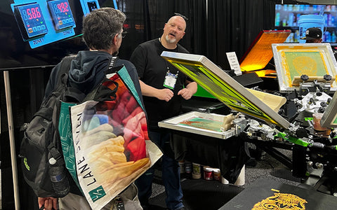 a man explains something to a customer holding a bag at a trade show