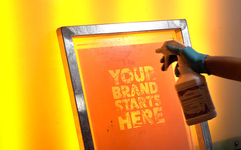 Una mano sostiene una botella de spray de removedor de emulsión en una pantalla en una cabina de lavado