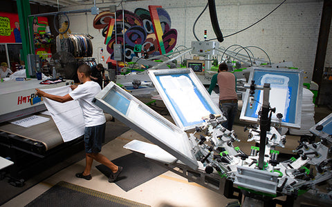 people work in a screen print shop with a manual and automatic press