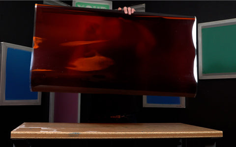 Una persona sostiene una película roja sobre una mesa en un cuarto oscuro.
