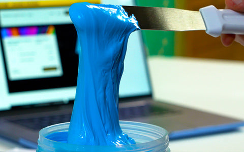 a hand holds an ink spatula dripping with blue ink