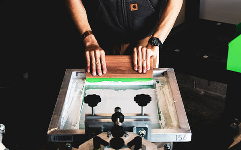 a printer's hands hold a squeegee, ready to push the squeegee over the screen